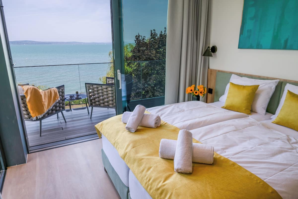A hotel room with a balcony, a bed with yellow bedding, and a view of the sea.