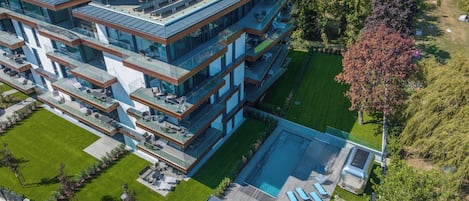 A modern multi-story building with a rooftop terrace, a swimming pool, and a well-maintained lawn.