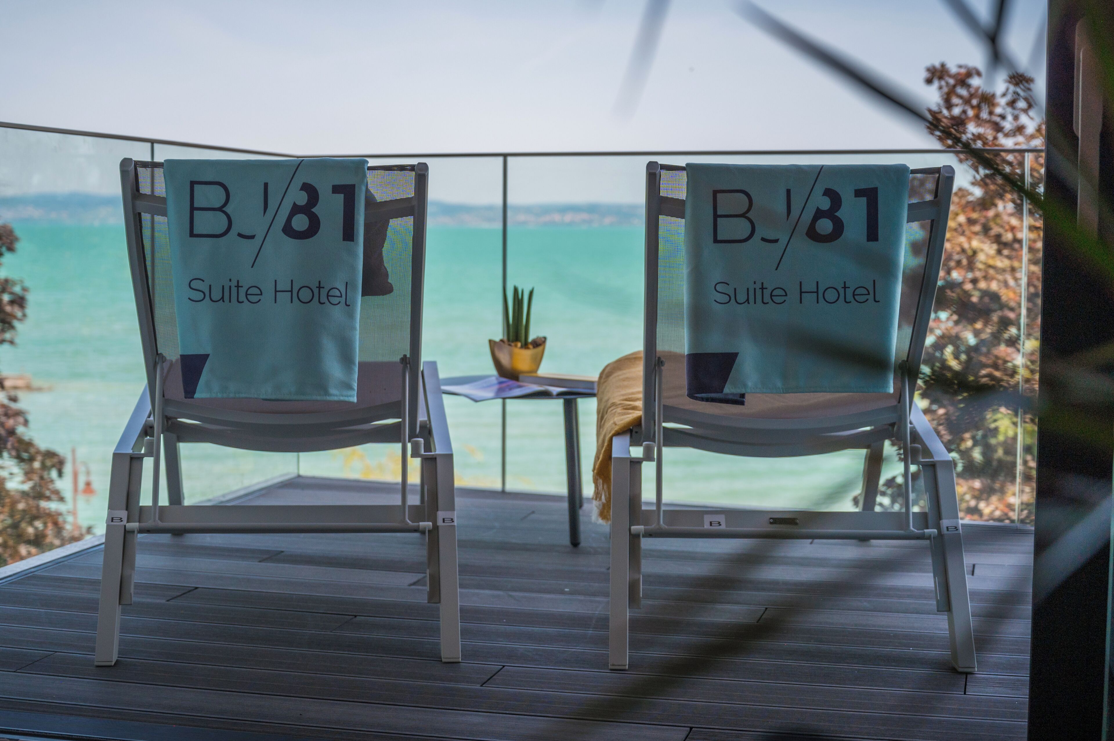 Due sedie con asciugamani del "B/81 Suite Hotel", un tavolino e una pianta in vaso su un balcone con vista sul mare.