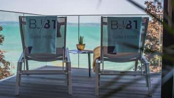 Due sedie con asciugamani del "B/81 Suite Hotel", un tavolino e una pianta in vaso su un balcone con vista sul mare.