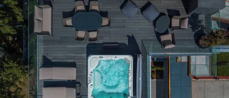 Vista aérea de una azotea con jacuzzi, mobiliario exterior y un área con cerramiento de vidrio.