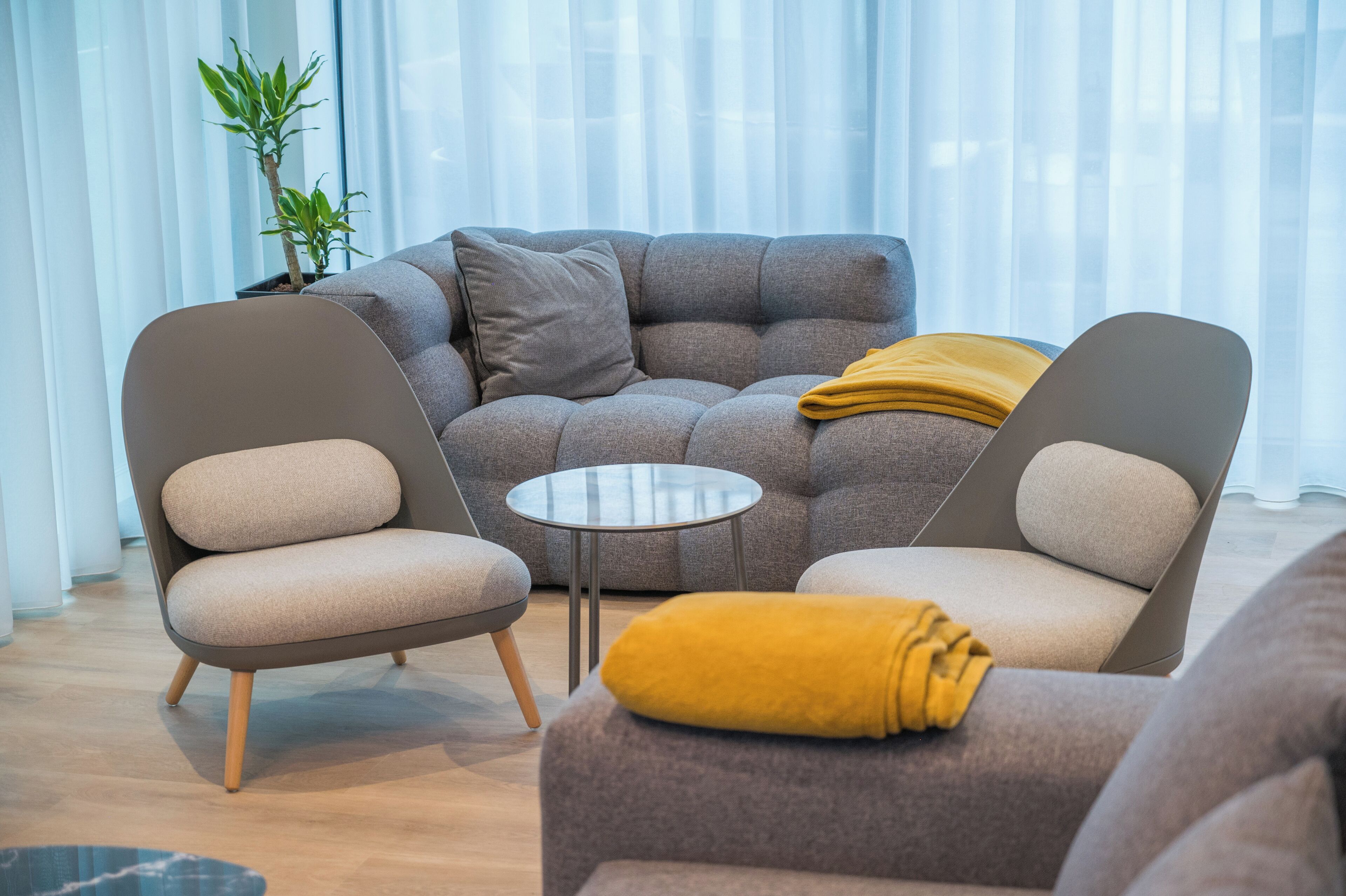 Una sala moderna con un sofá gris, dos sillones, una mesita redonda y una manta amarilla.