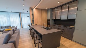 A modern kitchen with a central island, bar stools, and a dining area with a sofa and chairs. - BJ81 Suite Hotel (Siófok)