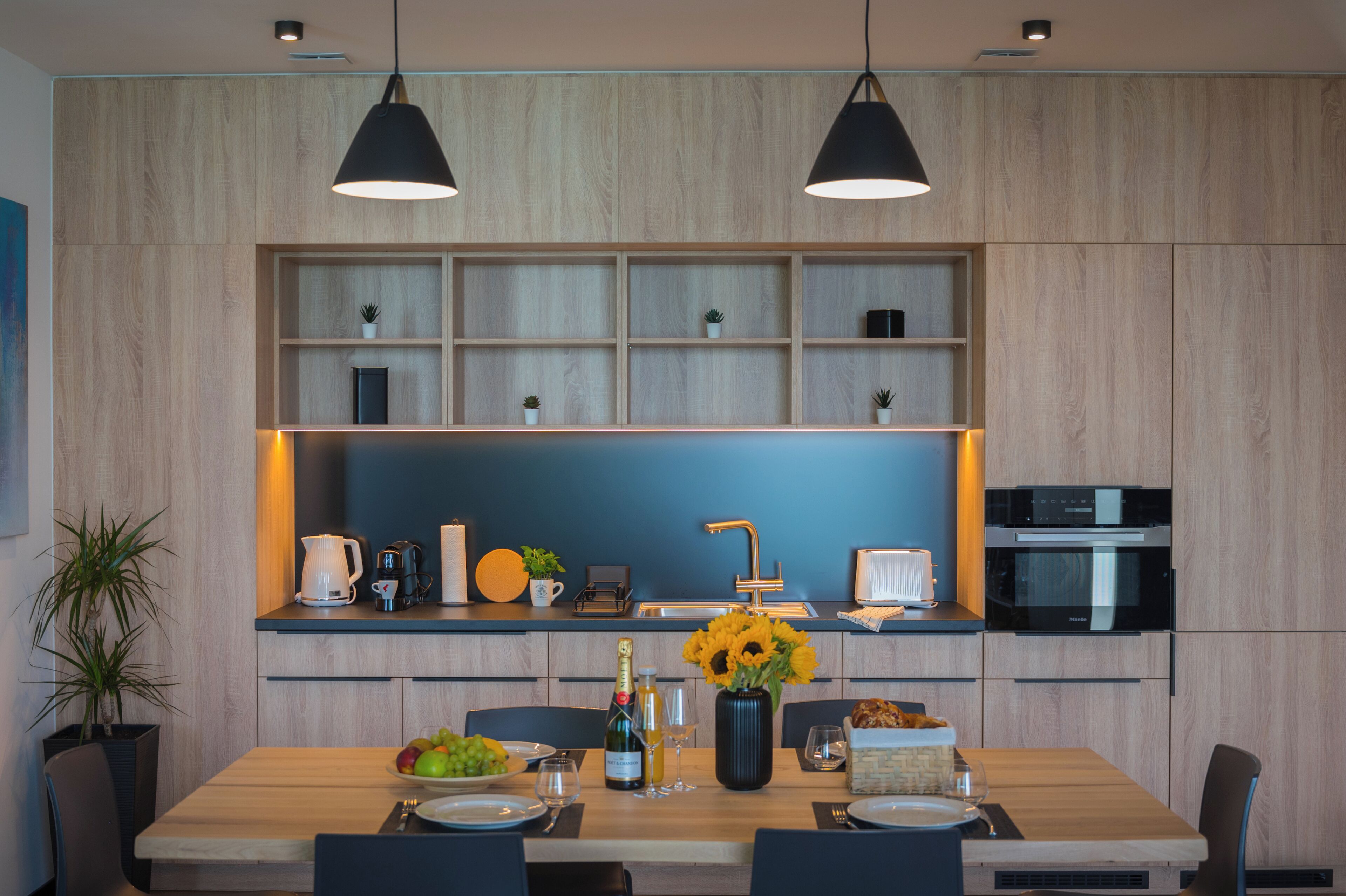 Een moderne keuken met houten kastjes, een inbouwoven en een eethoek met een houten tafel en stoelen.
