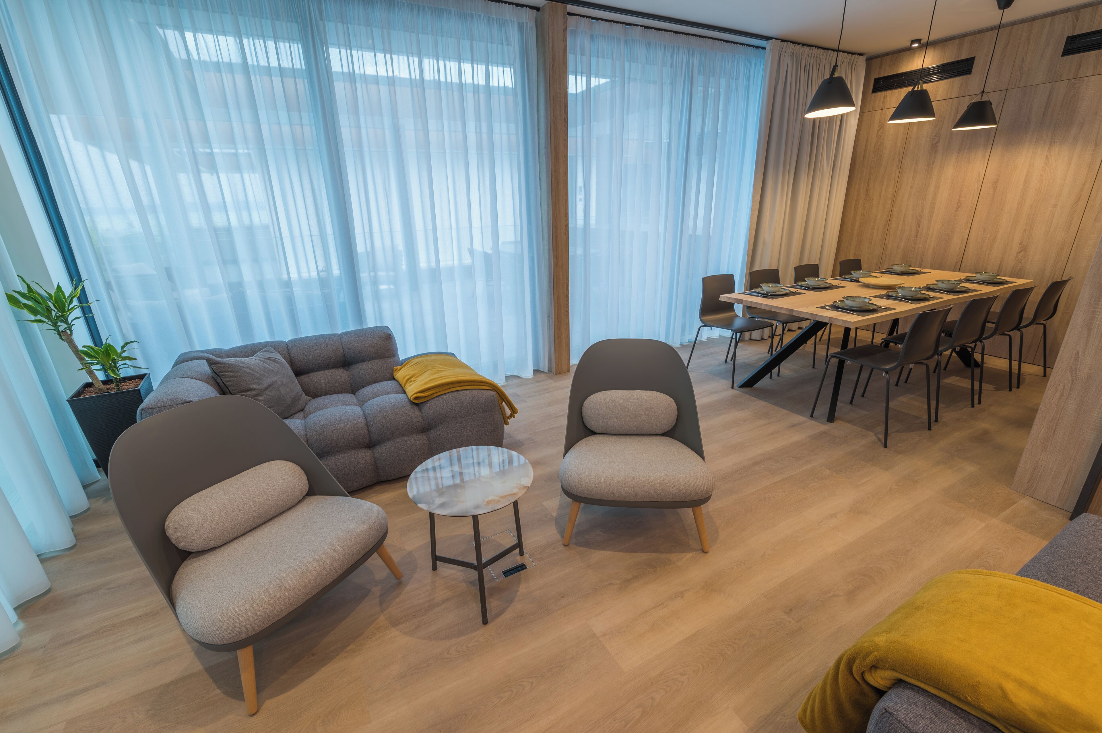 Un salon moderne comprenant un canapé, deux fauteuils, une petite table et un coin repas avec une table et des chaises.
