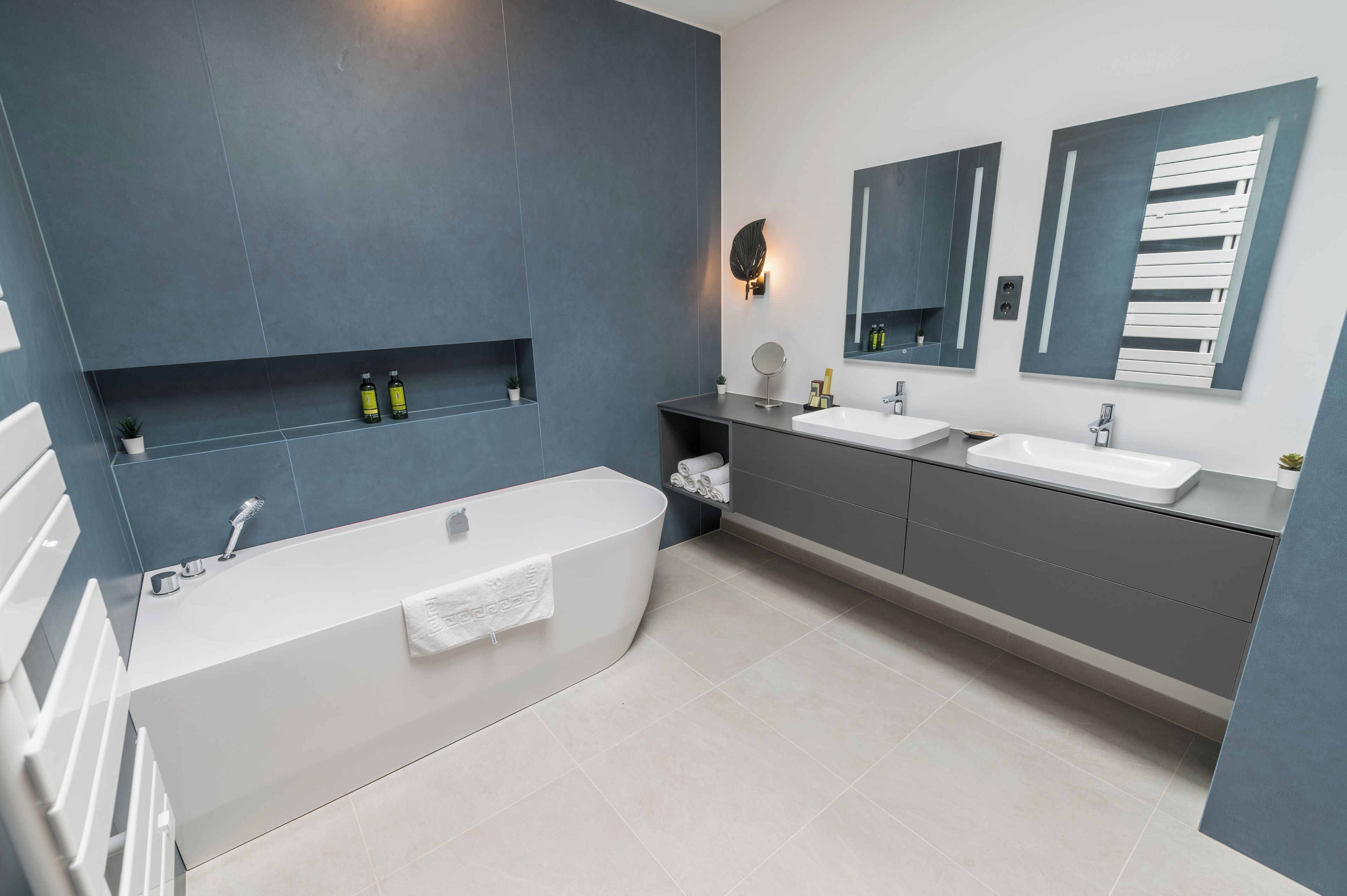 A modern bathroom with a bathtub, two sinks, and a large mirror.