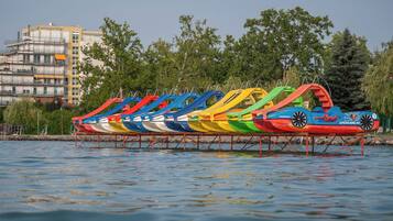 A row of colorful inflatable boats on a body of water with a building and trees in the background.