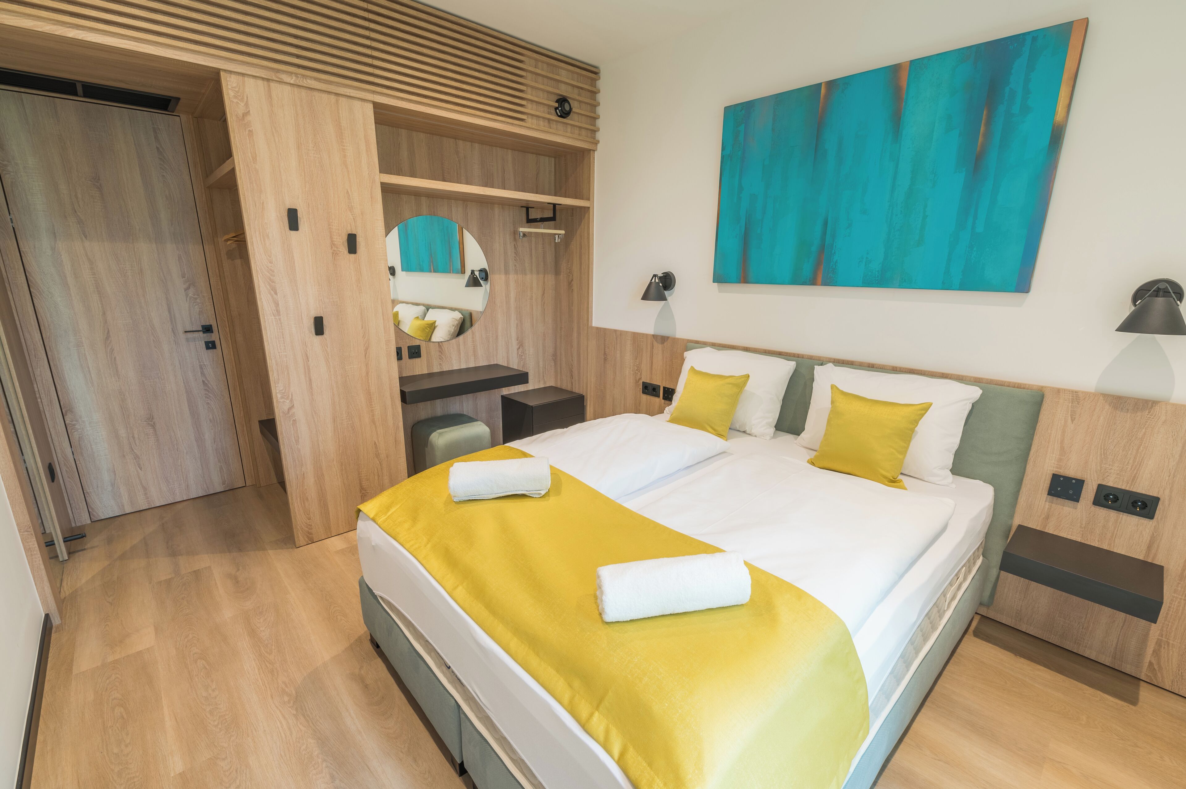 Ein modernes Hotelzimmer mit einem großen Bett, einem Schreibtisch, einem Spiegel und einem Gemälde an der Wand.
