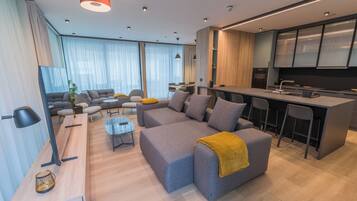 A modern living room with a grey sofa, a wooden coffee table, and a kitchen area with a bar and bar stools.