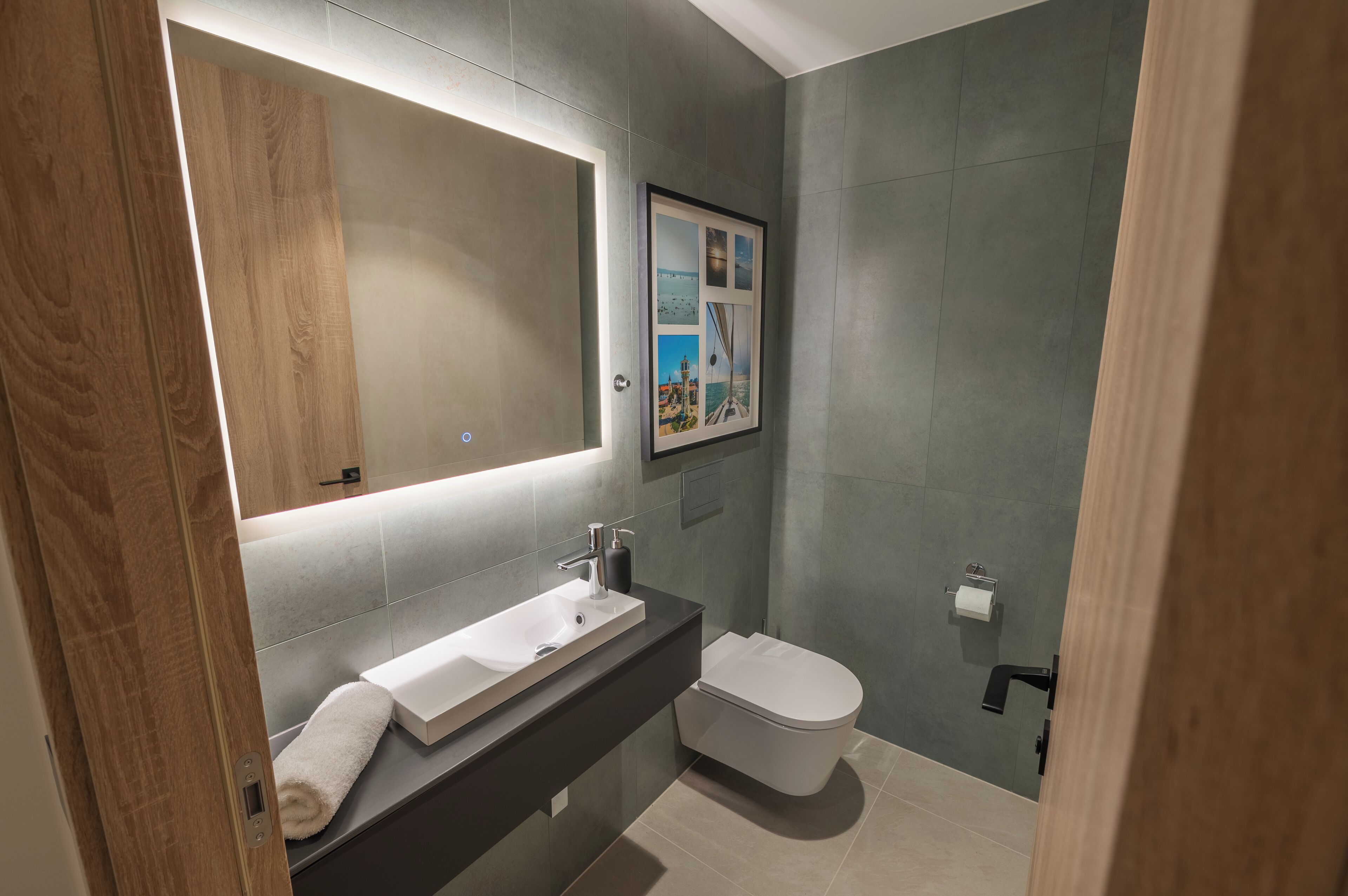 A modern bathroom with a wooden vanity, a large mirror, and a framed picture on the wall.