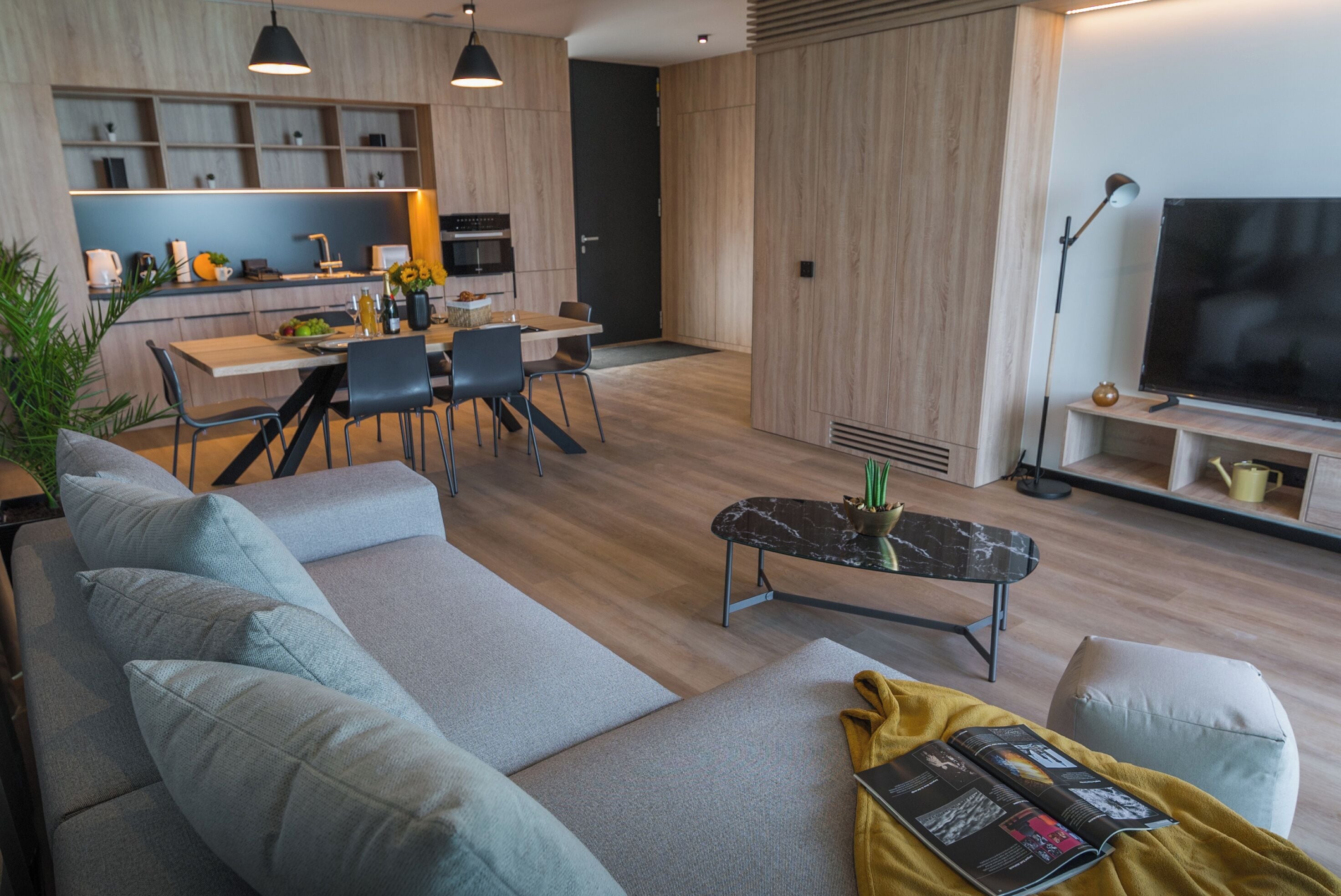 Ein modernes Wohnzimmer mit einer Couch, einem Couchtisch und einem Fernseher. Es gibt einen Essbereich mit Tisch und Stühlen.