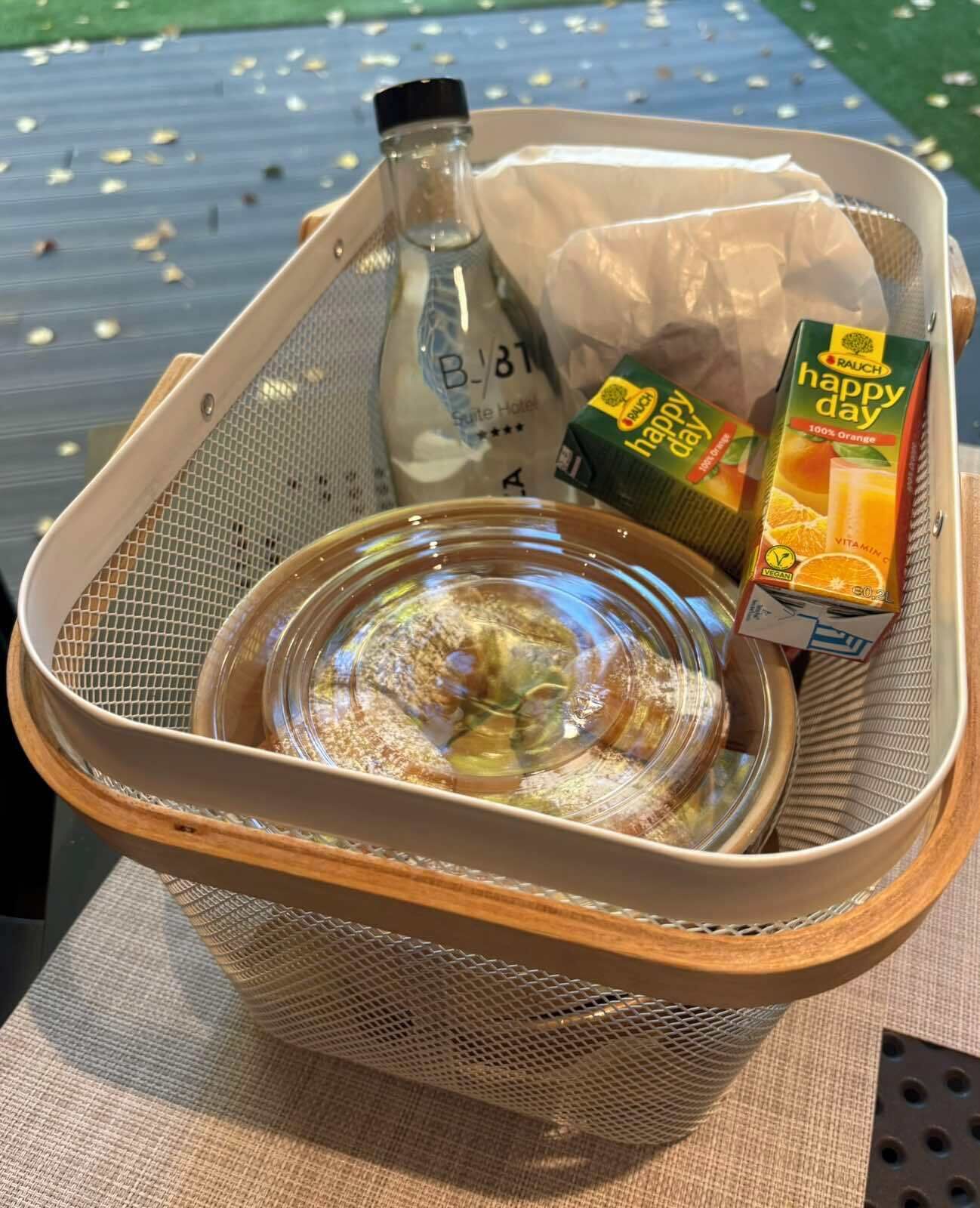A basket containing a bottle, a box of orange juice, and a glass bowl.