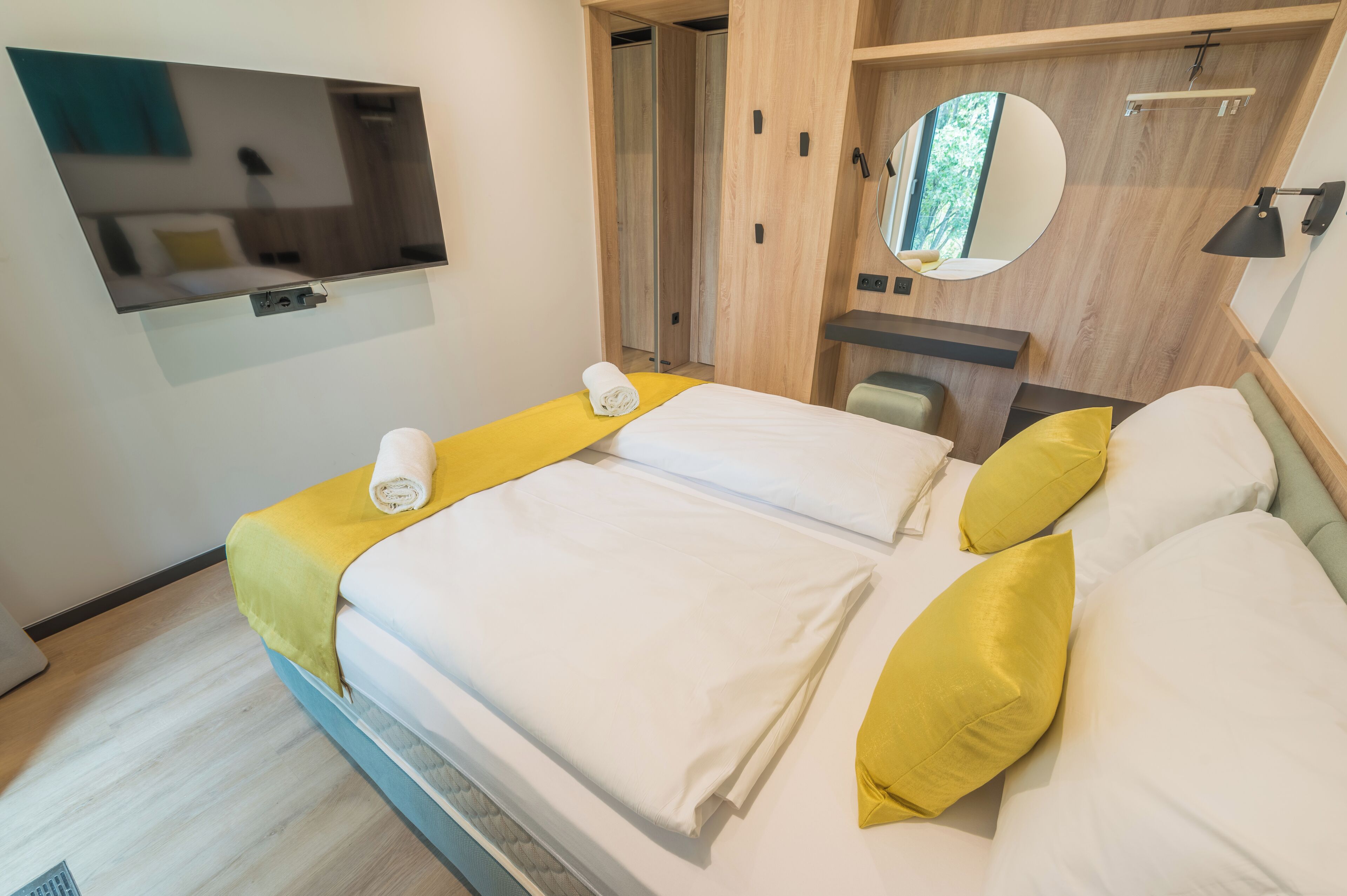 A hotel room with a bed, a TV mounted on the wall, a mirror, and a small desk.