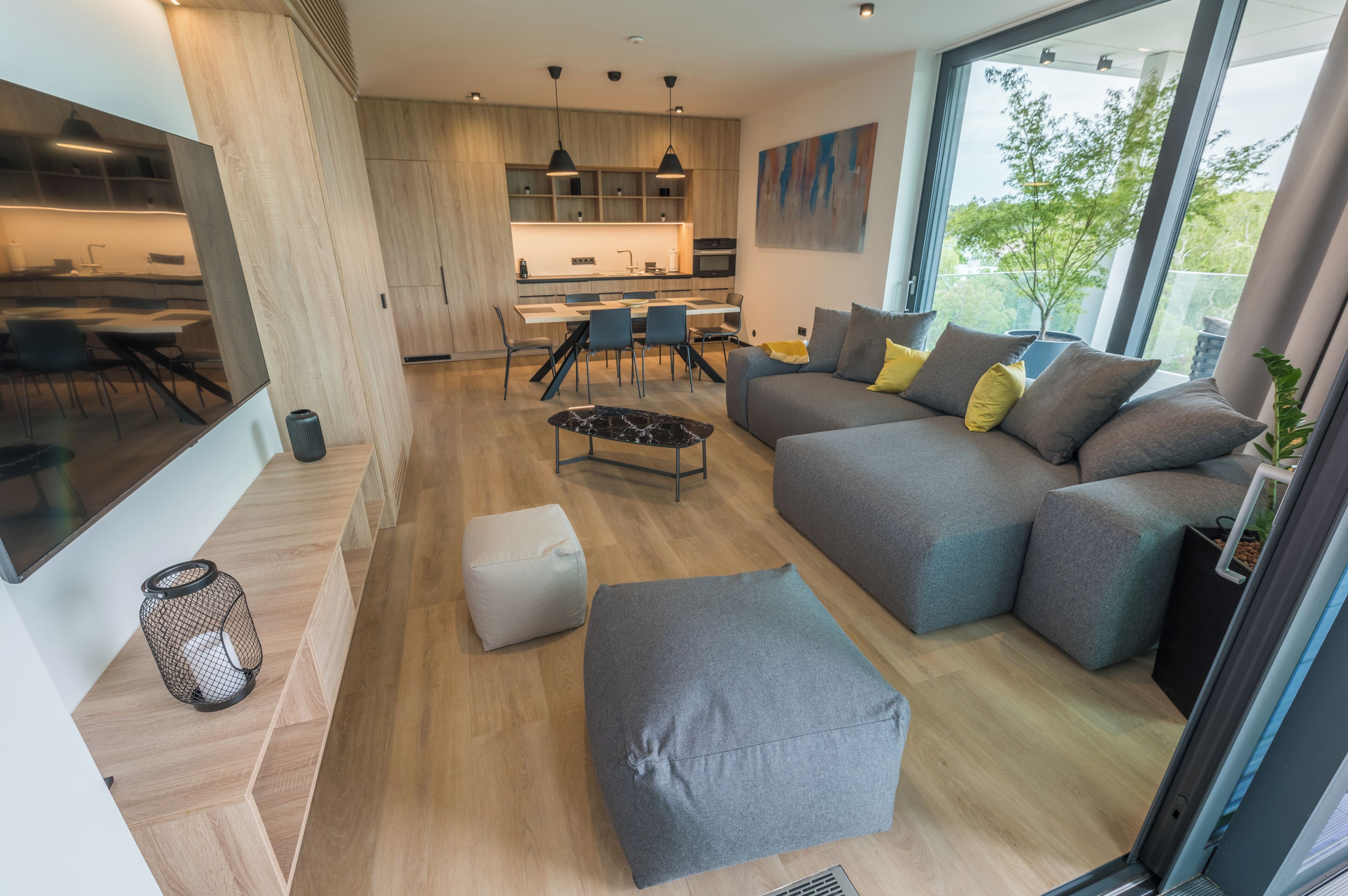 Una sala moderna con un sofá gris, un reposapiés y un comedor con sillas y una mesa.