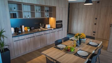 Cocina moderna con armarios de madera, una mesa de comedor para dos personas y un frutero.