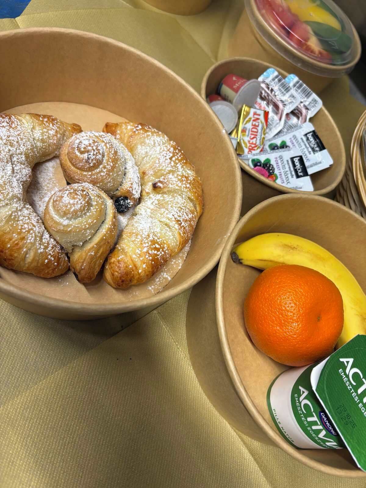A bowl of pastries with a banana and an orange, and a container of yogurt.
