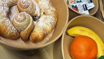 A bowl of pastries with a banana and an orange, and a container of yogurt.
