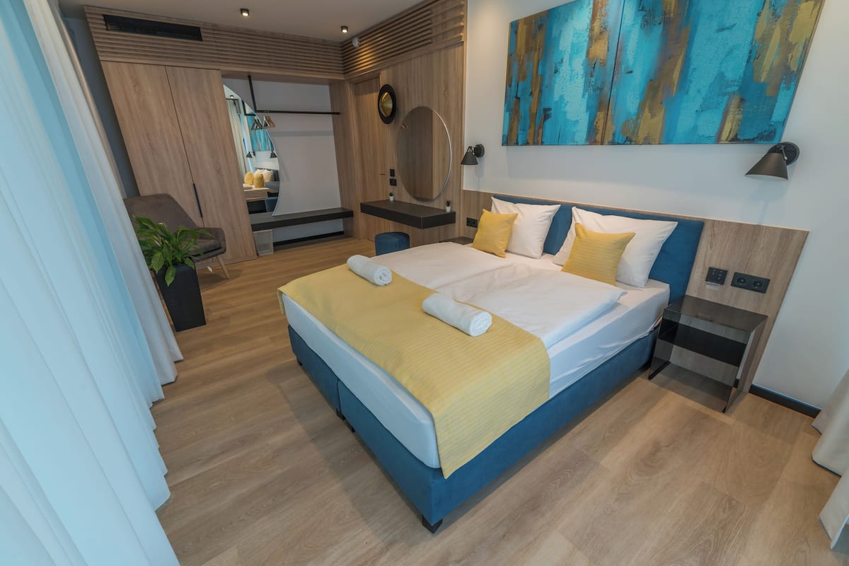 A modern hotel room with a large bed, a bedside table, a mirror, and a wall-mounted artwork.