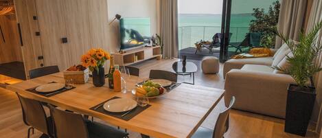 Una sala de estar moderna con comedor, televisor y balcón con vista al mar.