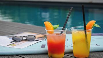 Two drinks with straws and orange slices on a table near a pool.