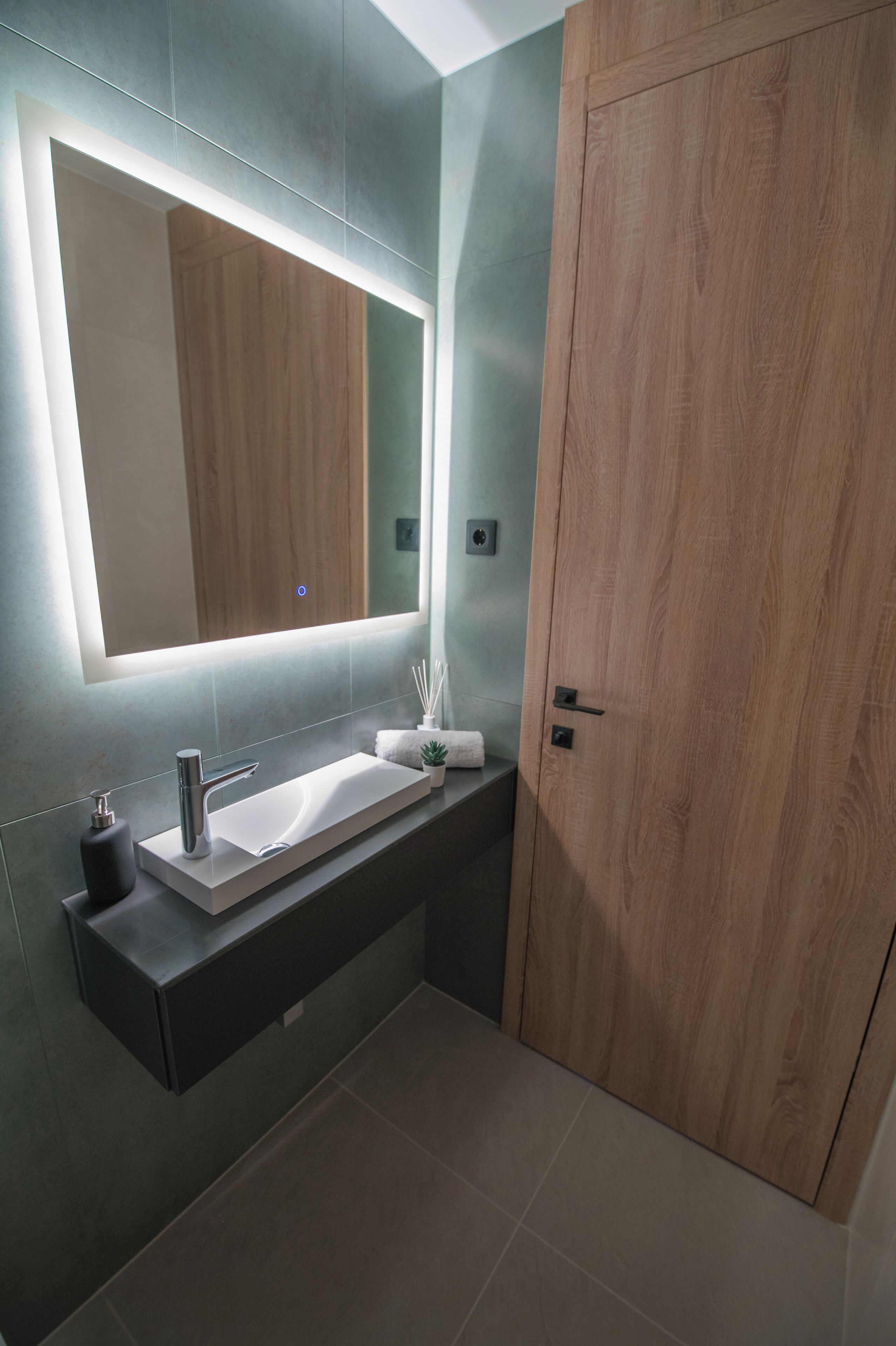 A modern bathroom with a large mirror, a white sink, and a wooden door.
