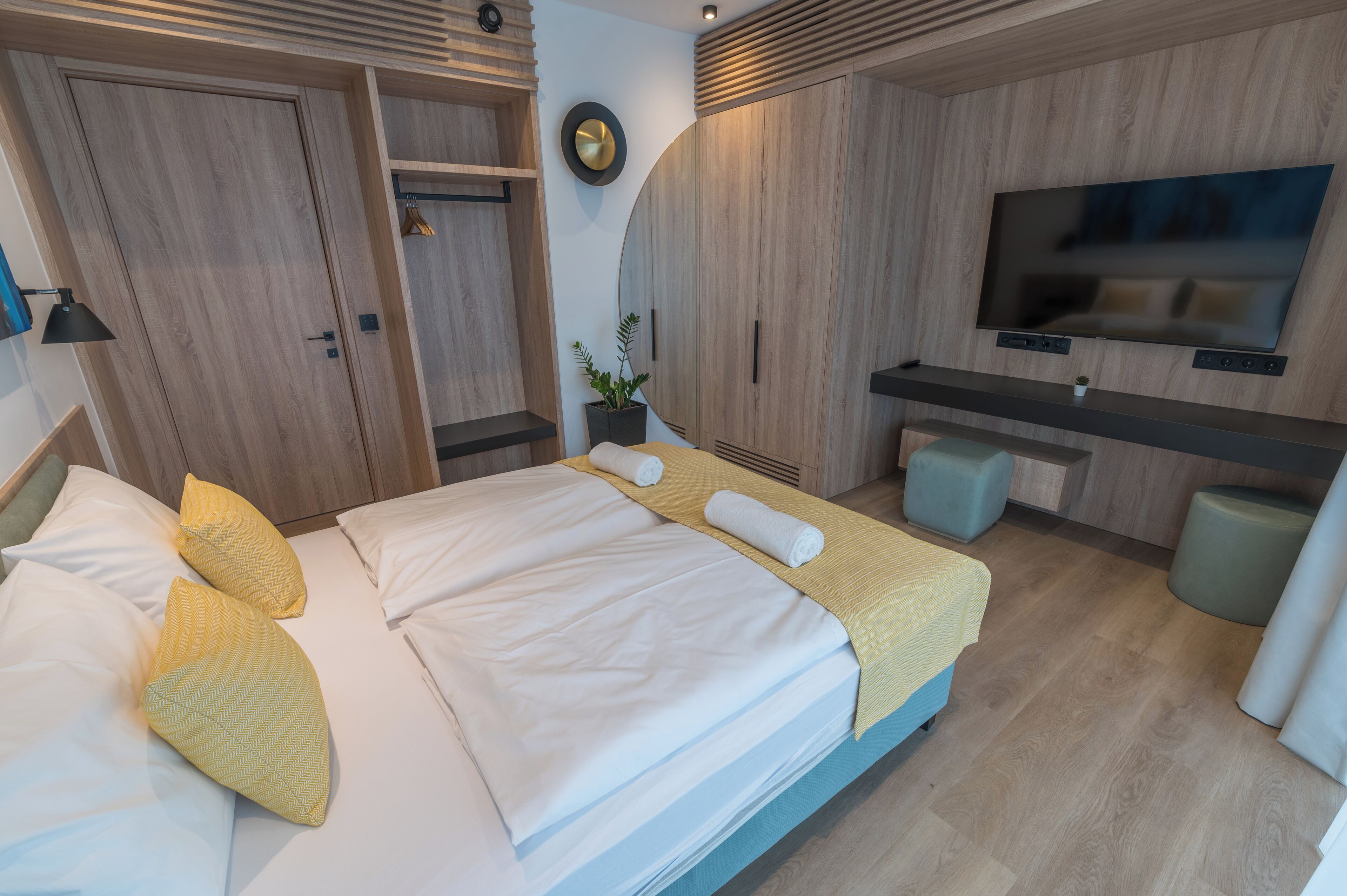Una habitación de hotel moderna con cama, mesitas de noche, televisor y un pequeño rincón de descanso.