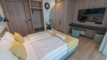 A modern hotel room with a bed, bedside tables, a TV, and a small seating area.