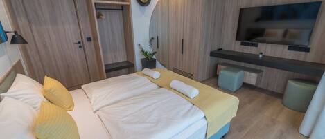 Una habitación de hotel moderna con cama, mesitas de noche, televisor y un pequeño rincón de descanso.