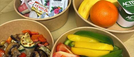 A meal setup with bowls containing vegetables, a basket of bread, and a carton of orange juice.
