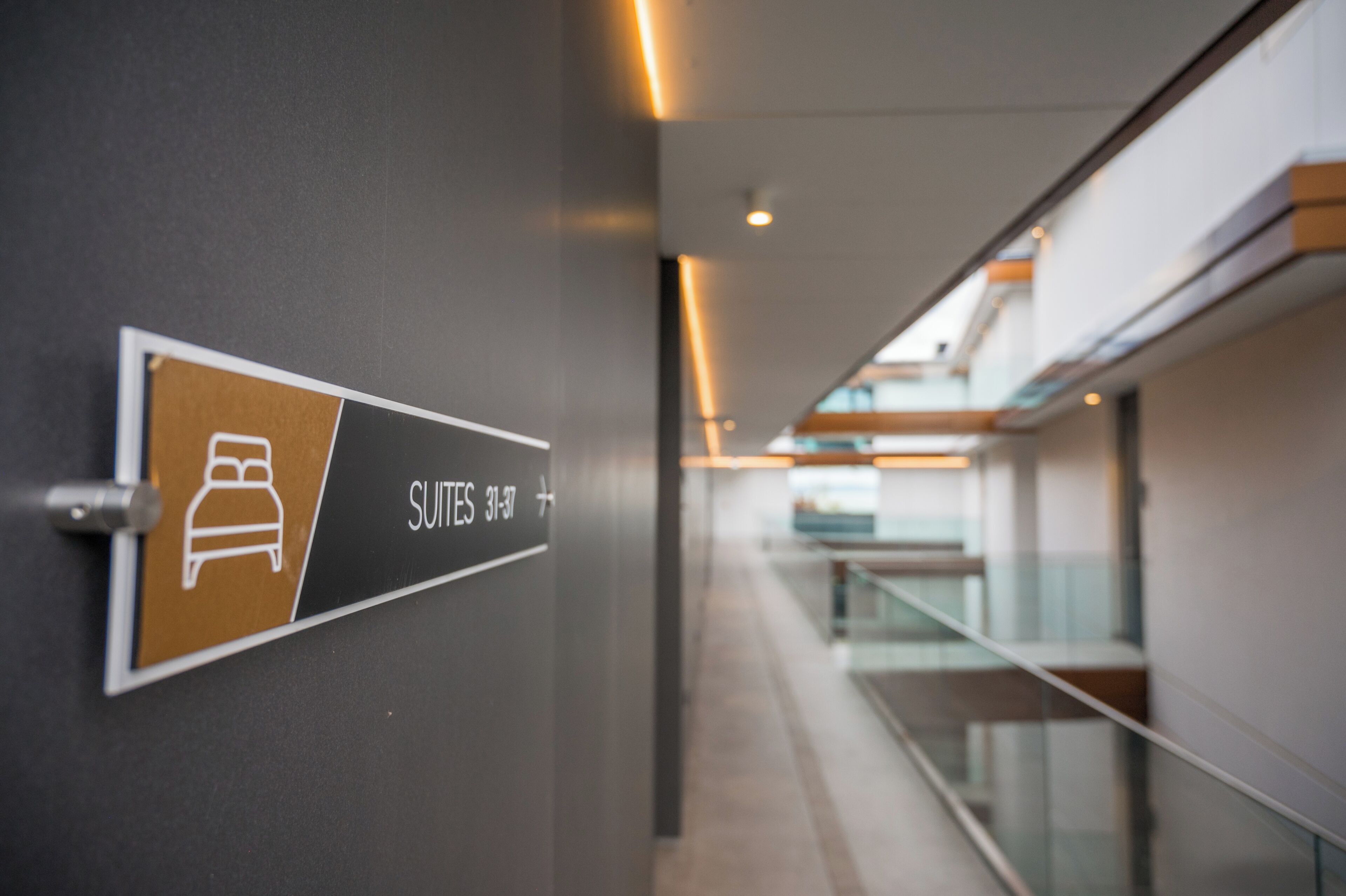 Segnaletica che indica la posizione delle suite 31-37 in un edificio moderno con ringhiera in vetro e vista sull'interno.