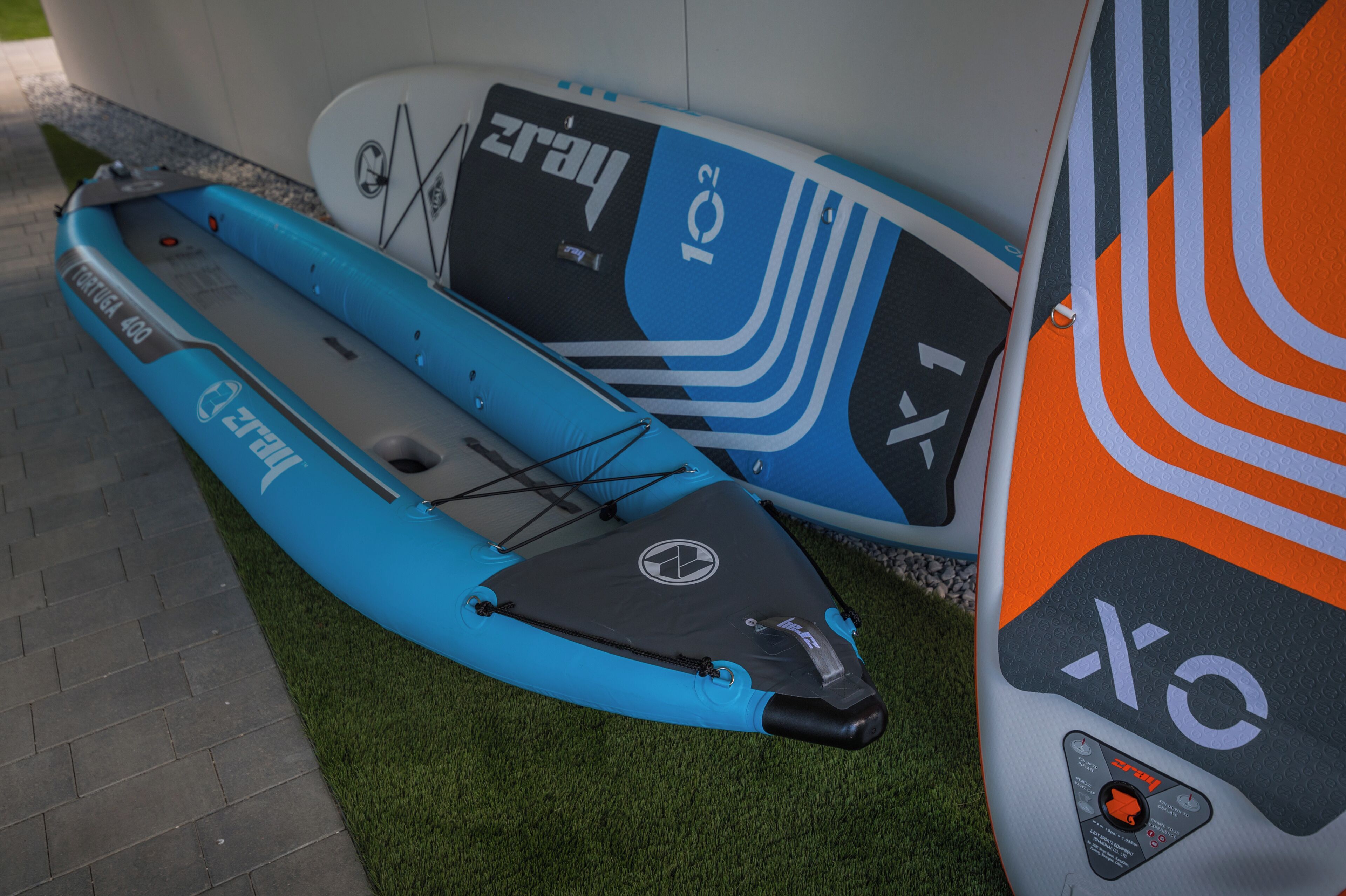 Dos kayaks de diseños y logotipos diferentes, sobre césped artificial cerca de una pared.