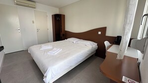 A hotel room with a bed, a desk, a chair, a wardrobe, and an air conditioning unit. - Halte Hotel (La Vergne)