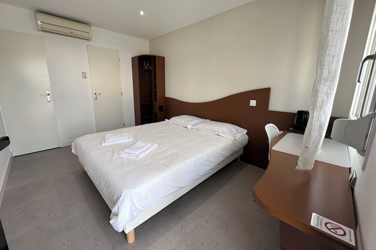 Ein Hotelzimmer mit Bett, Schreibtisch, Stuhl, Kleiderschrank und Klimaanlage.