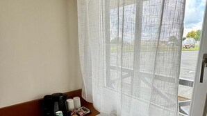 A small hotel room with a wooden desk, a white chair, a coffee maker, and a window with sheer curtains. - Halte Hotel (La Vergne)