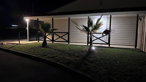 A modern building with a covered patio area, palm trees, and a well-maintained lawn. - Halte Hotel (La Vergne)