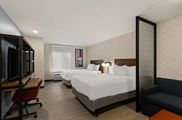 A hotel room with two beds, a desk with a computer, a TV, a sofa, and a decorative wall panel.