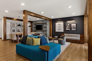 Un salon moderne avec un canapé bleu, des poutres en bois, un coin repas et un mur décoré de tableaux encadrés et d’une citation inspirante.
