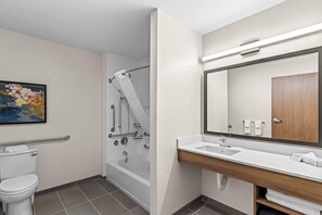A bathroom with a toilet, shower, sink, and a large mirror.