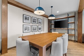 Una sala de conferencias con una mesa de madera, sillas grises, un televisor en un estante y cuadros en la pared.