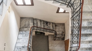 Un escalier en marbre avec une rampe métallique, une vue sur l’étage inférieur et une lucarne au-dessus.
