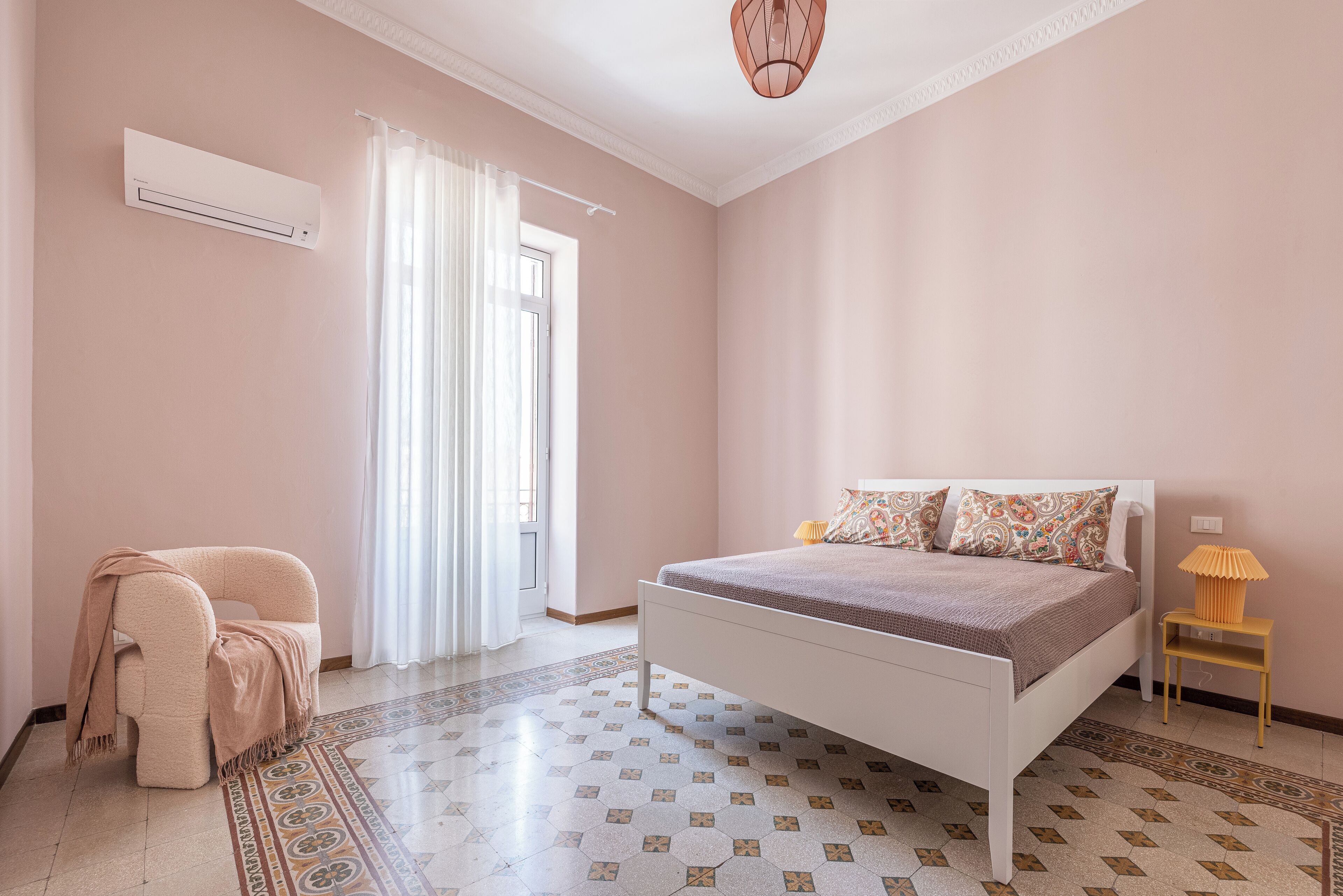 Un dormitorio con cama, una silla, una lámpara y un ventanal con cortinas.