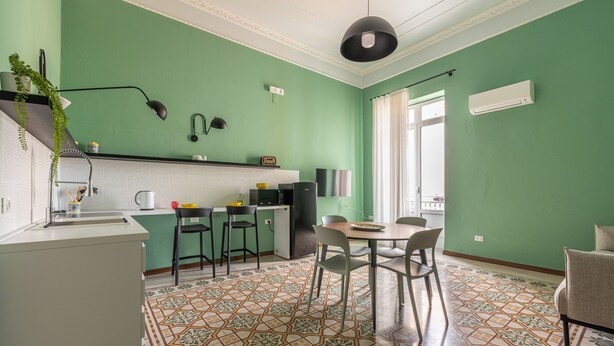 Une cuisine moderne avec un mur vert, des armoires blanches et un sol carrelé à motifs.