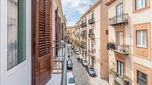 Une rue étroite, bordée de bâtiments des deux côtés, avec des balcons ornés de plantes et où du linge est étendu pour sécher.