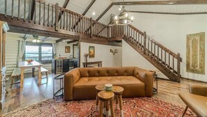 A spacious living area with a high ceiling, a wooden staircase, a leather sofa, and a patterned rug.