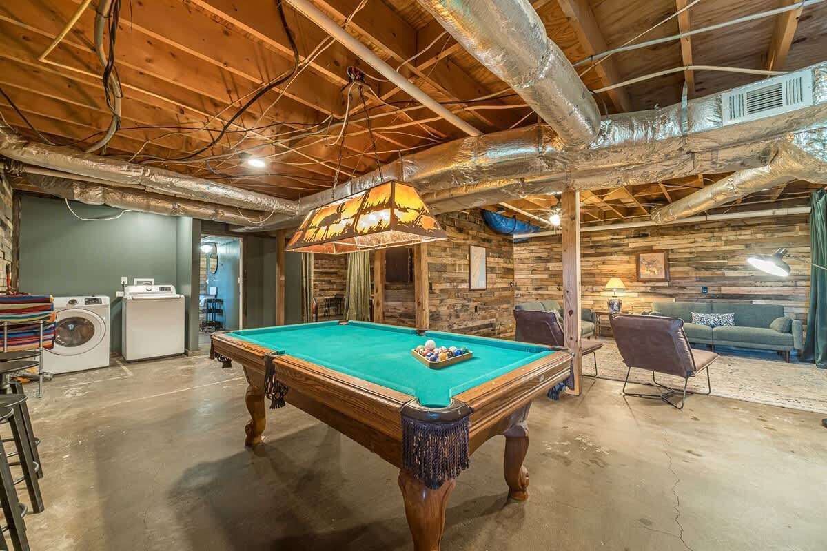 A pool table in a room with exposed wooden beams, a washing machine, and a couch.