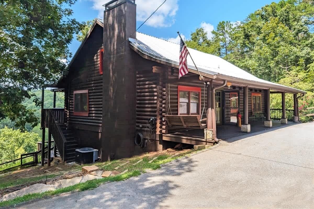 A rustic log cabin with a porch, a chimney, and an American flag.