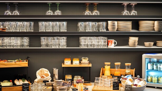 A kitchen area with shelves of glassware, a refrigerator, and various kitchen appliances. - HOTEL andrä (Salzburg)