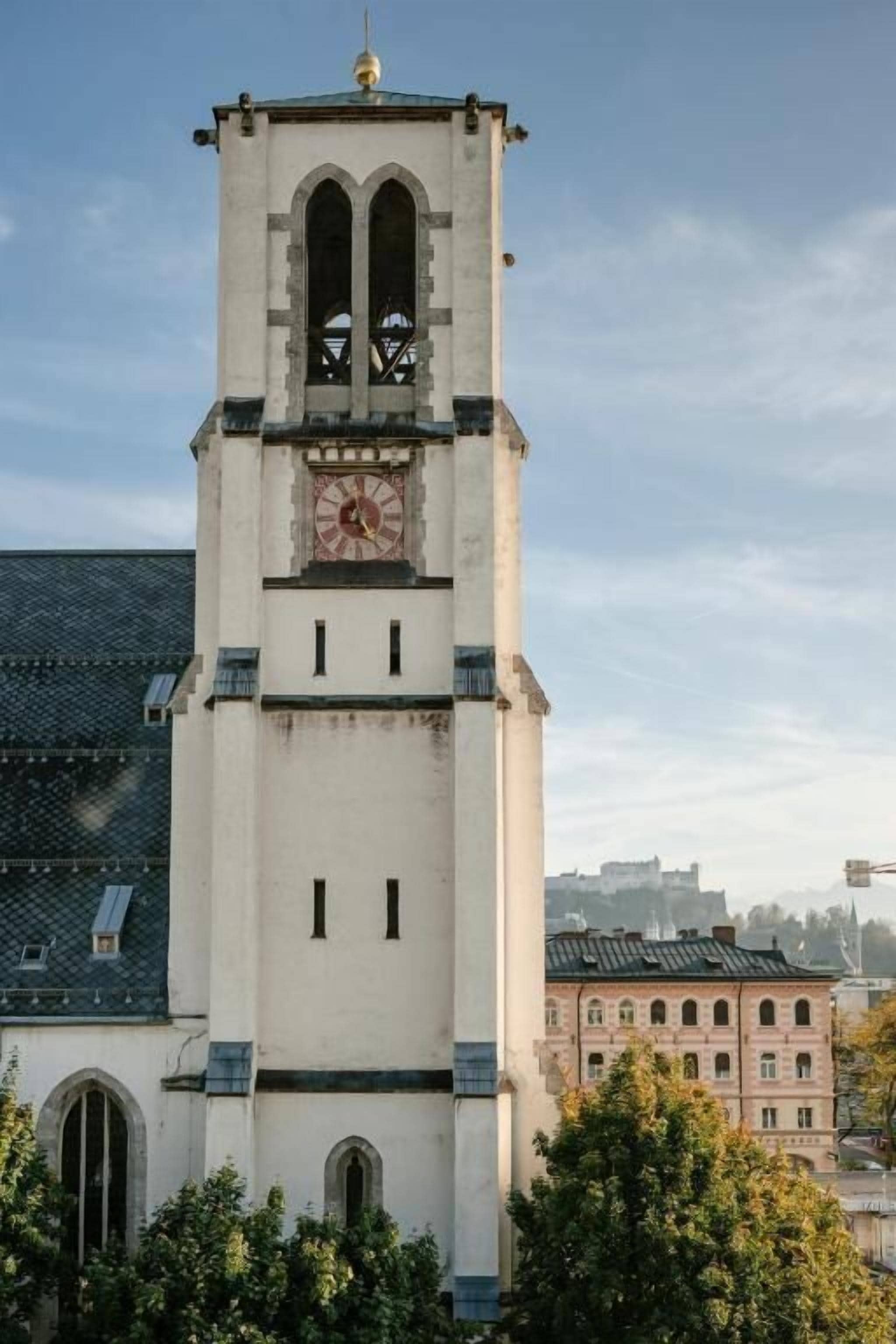 Una alta torre de reloj con esfera horaria, ventanas arqueadas y un techo puntiagudo.