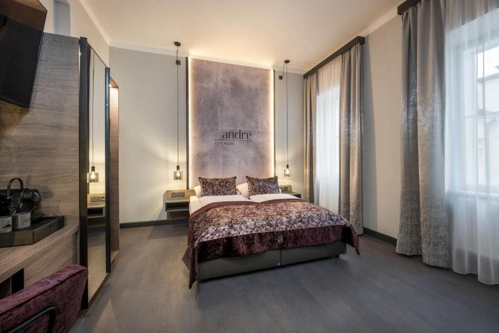 A modern hotel room with a large bed, bedside tables, a mirror, and a wall-mounted sign.