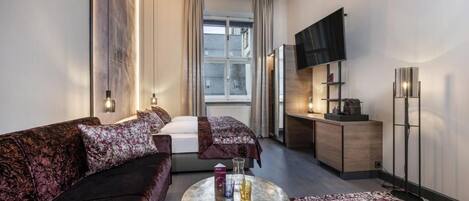 Una habitación de hotel moderna con sofá, una mesita redonda, cama, televisor y escritorio.